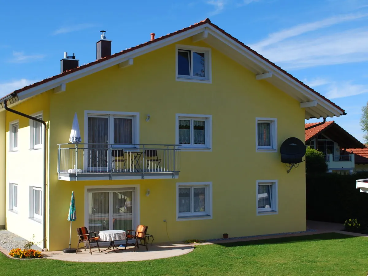 Das gelbe Haus der Familie Bergmann im Sommer: Balkon im ersten Stock, darunter Terrasse und Rasen